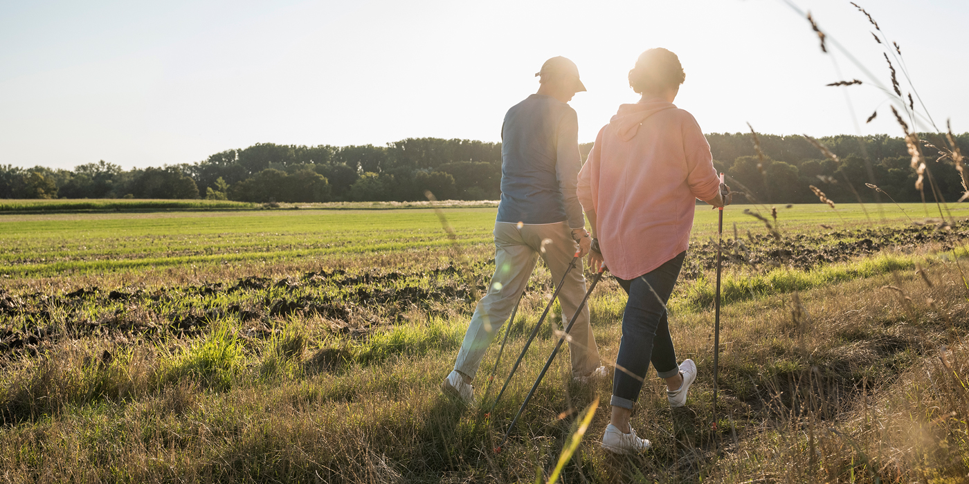Older adults walking outdoors with trekking poles at sunset