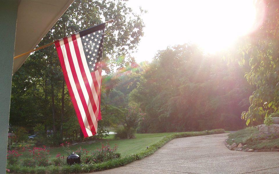 American flag displayed outside near trees and a sunlit driveway