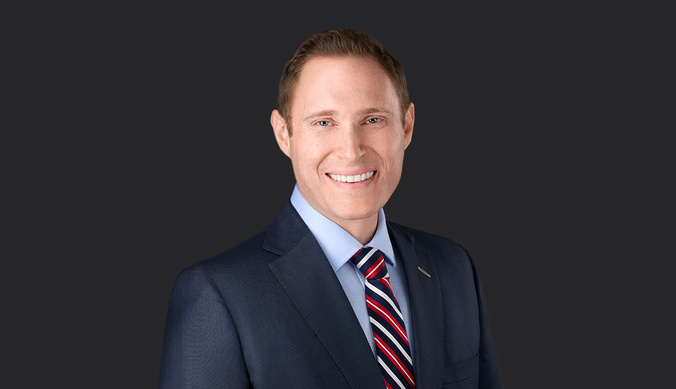 Professional man in a navy suit and striped tie smiling against a dark studio background
