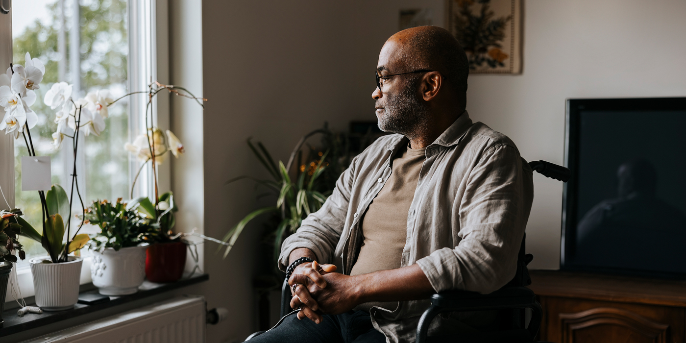 Man sitting thoughtfully in a wheelchair by a window at home