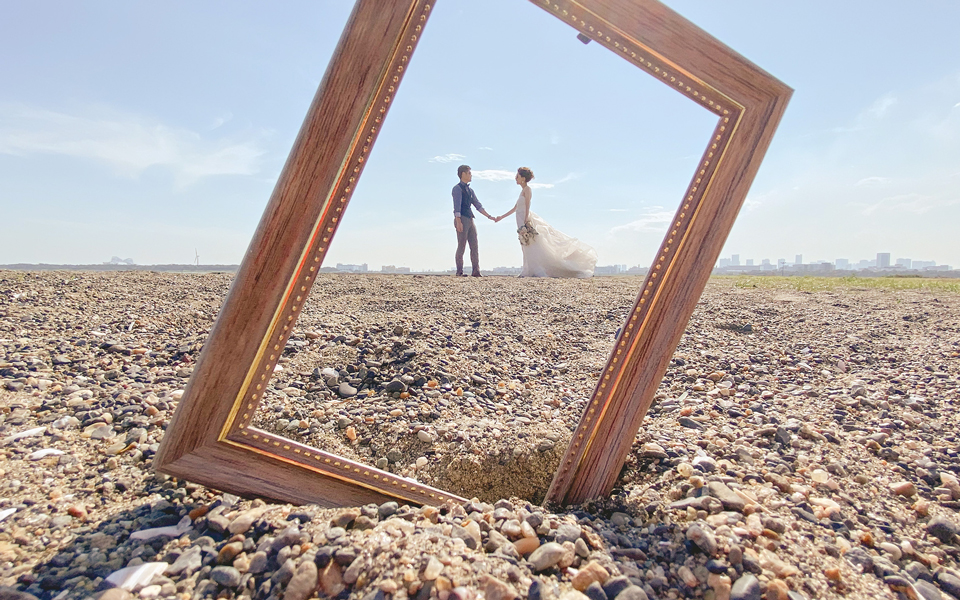 Wedding couple framed inside an empty picture frame on a beach