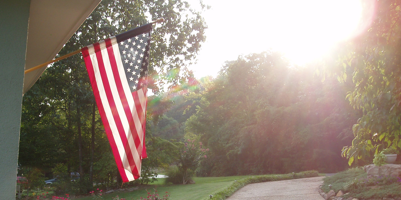 American flag displayed outside near trees and a sunlit driveway