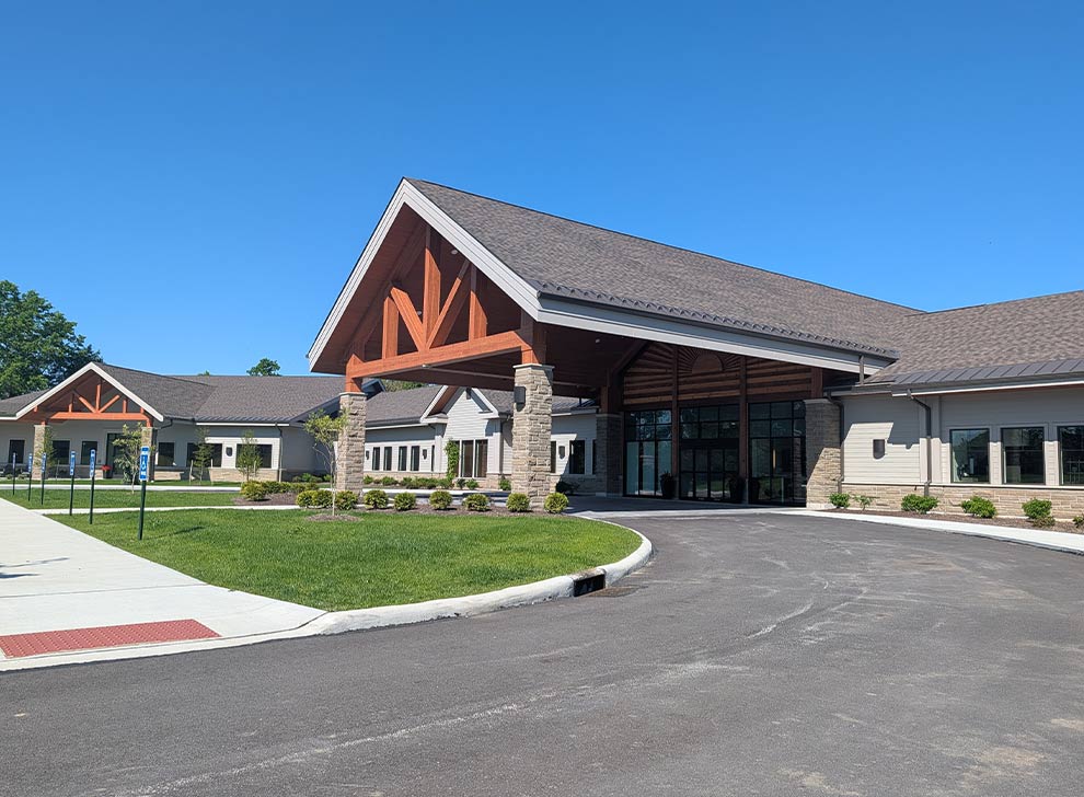 Exterior view of a modern lakeside hospice or healthcare facility with covered entrance and landscaped grounds
